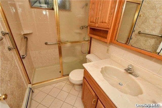 bathroom featuring tile patterned floors, vanity, a shower with door, a baseboard radiator, and toilet