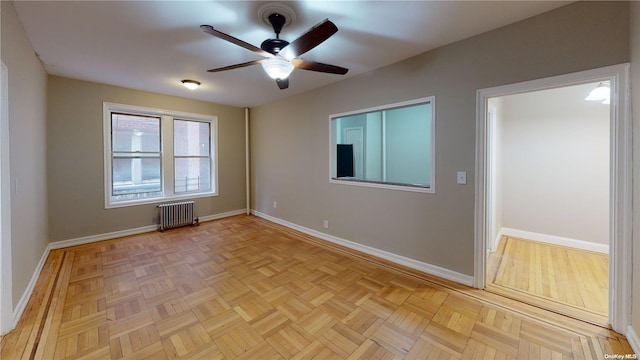 empty room with ceiling fan, radiator heating unit, and light parquet flooring