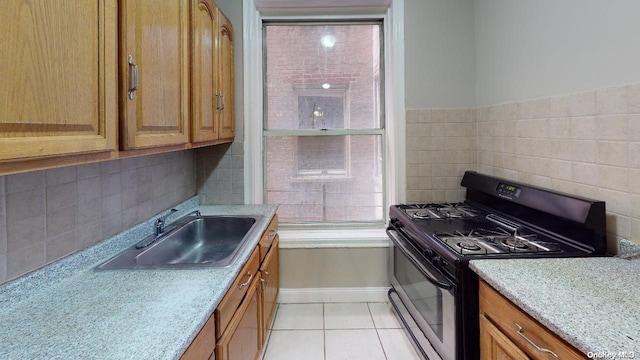 kitchen featuring black gas stove, light tile patterned floors, tile walls, and sink