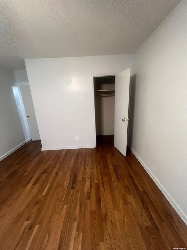 unfurnished bedroom featuring a textured ceiling, dark hardwood / wood-style floors, and a closet