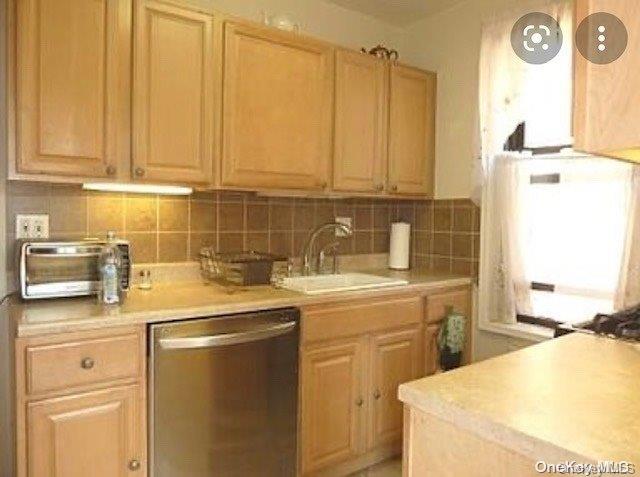 kitchen featuring stainless steel dishwasher, backsplash, light brown cabinets, and sink