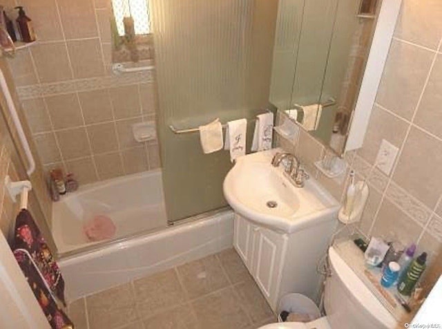 full bathroom with tile patterned flooring, combined bath / shower with glass door, toilet, vanity, and tile walls