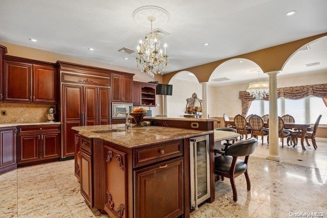 kitchen with decorative columns, a kitchen island with sink, sink, a notable chandelier, and hanging light fixtures