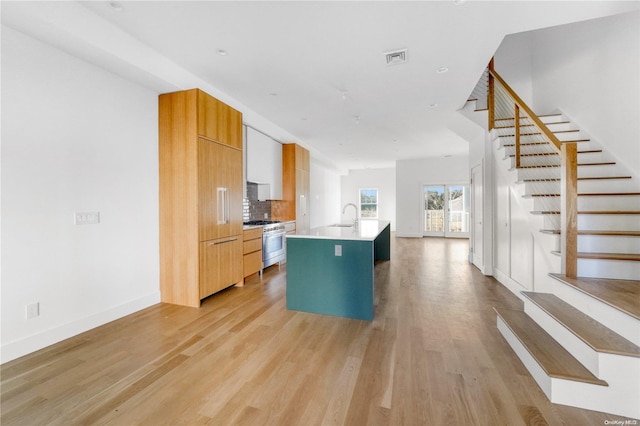 kitchen with sink, light hardwood / wood-style flooring, an island with sink, decorative backsplash, and high end stainless steel range