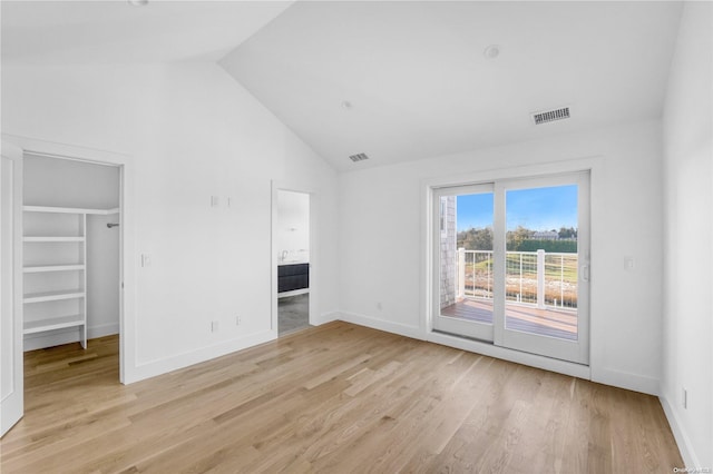 unfurnished bedroom with high vaulted ceiling, access to outside, a walk in closet, light hardwood / wood-style floors, and a closet