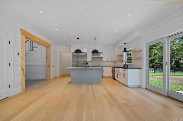 kitchen featuring white cabinetry, stainless steel appliances, a kitchen island, decorative light fixtures, and light wood-type flooring