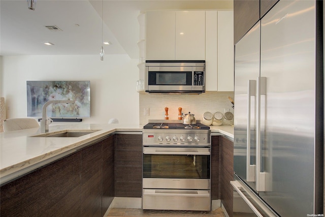 kitchen with high quality appliances, white cabinets, sink, light stone countertops, and dark brown cabinetry