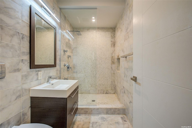 bathroom featuring a tile shower, vanity, and tile walls