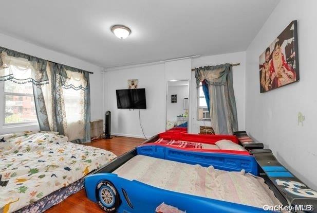 bedroom with hardwood / wood-style flooring, radiator heating unit, and multiple windows