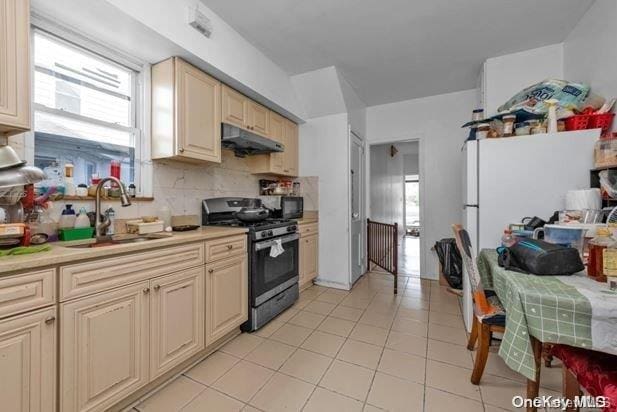 kitchen featuring cream cabinets, stainless steel range with gas cooktop, sink, decorative backsplash, and light tile patterned flooring