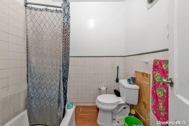 bathroom featuring hardwood / wood-style flooring, toilet, tile walls, and shower / tub combo