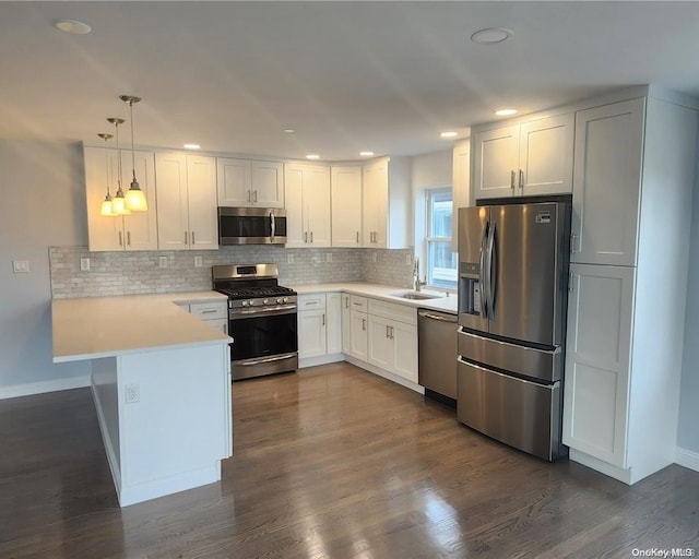 kitchen featuring kitchen peninsula, appliances with stainless steel finishes, dark hardwood / wood-style floors, white cabinetry, and hanging light fixtures