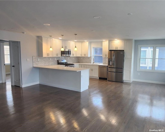 kitchen with kitchen peninsula, appliances with stainless steel finishes, hanging light fixtures, and a healthy amount of sunlight