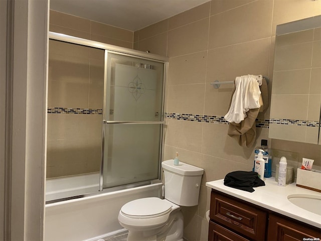 full bathroom with shower / bath combination with glass door, vanity, tile walls, and toilet