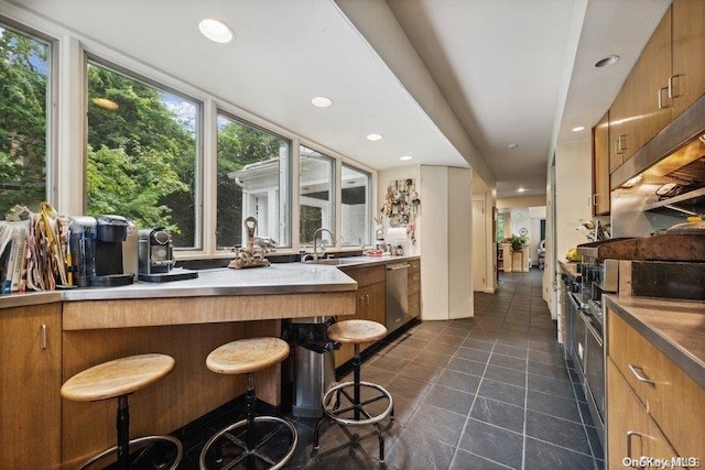 kitchen featuring a kitchen bar, sink, stainless steel dishwasher, and dark tile patterned flooring