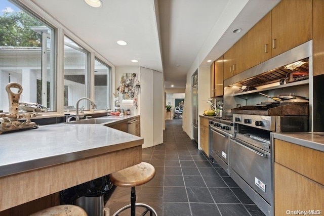 kitchen with a kitchen bar, ventilation hood, high end fridge, and sink