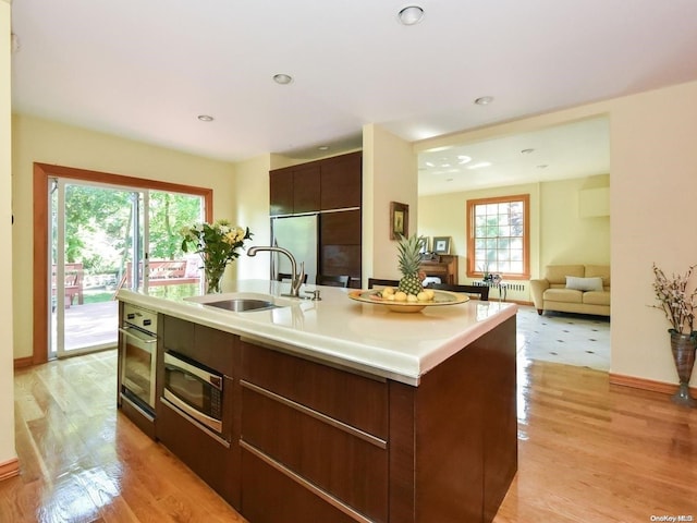 kitchen with a center island with sink, sink, light hardwood / wood-style flooring, appliances with stainless steel finishes, and dark brown cabinetry