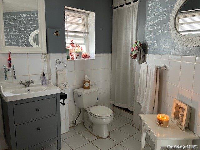 bathroom featuring tile patterned flooring, vanity, toilet, and tile walls