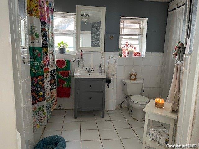 bathroom with tile patterned flooring, vanity, toilet, and tile walls