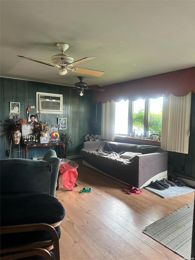 living room featuring a wall mounted air conditioner, ceiling fan, hardwood / wood-style floors, and wooden walls