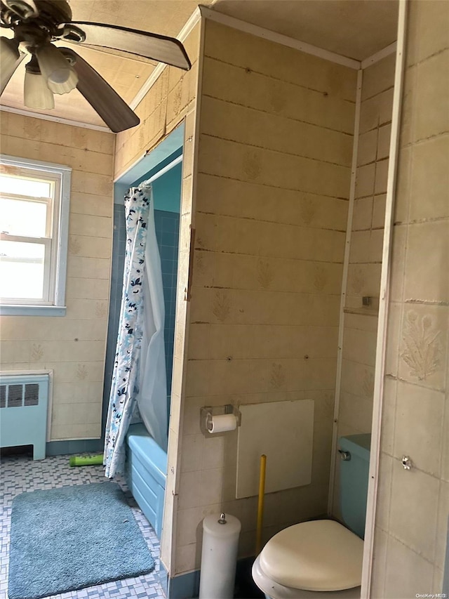 bathroom with shower / bath combo, wood walls, ceiling fan, toilet, and radiator heating unit