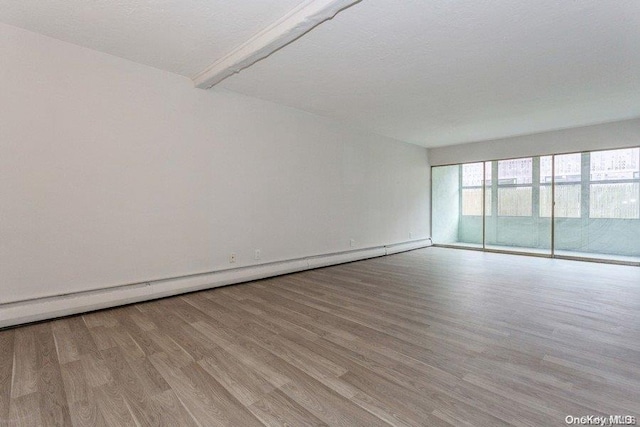 unfurnished room with beam ceiling, light hardwood / wood-style floors, a textured ceiling, and a baseboard heating unit