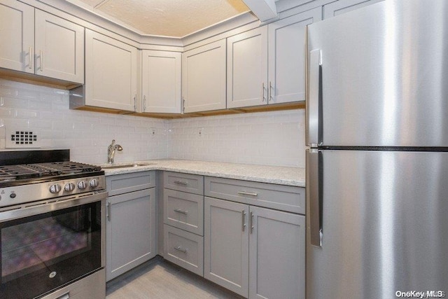 kitchen with gray cabinetry, sink, stainless steel appliances, light stone counters, and decorative backsplash