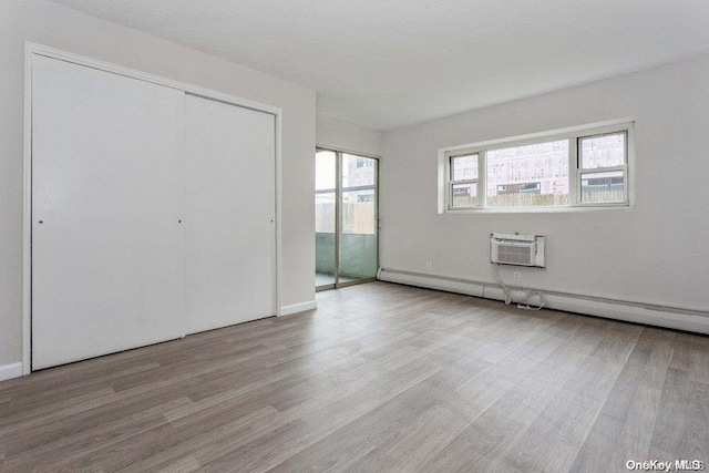 unfurnished bedroom with a wall mounted AC, a closet, light hardwood / wood-style flooring, and a baseboard heating unit