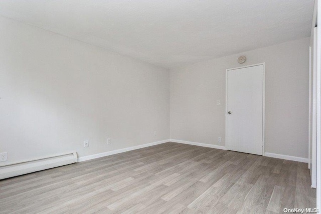 spare room with baseboard heating and light hardwood / wood-style floors