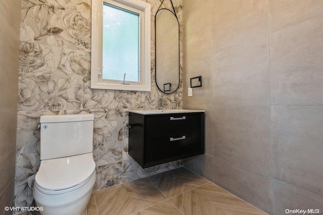 bathroom with vanity, toilet, parquet floors, and tile walls