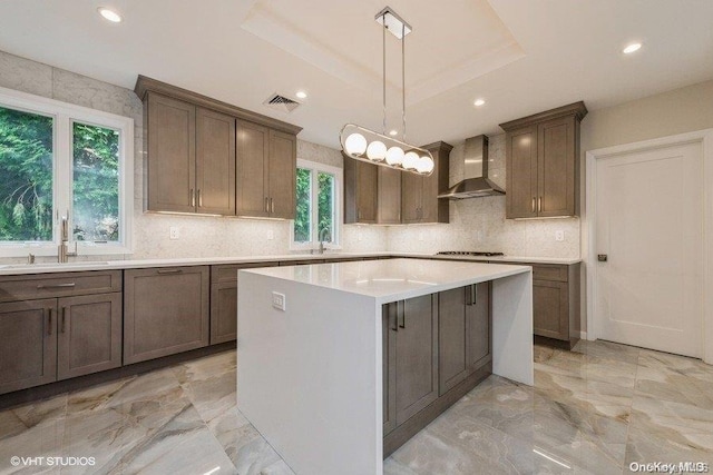 kitchen featuring a center island, wall chimney exhaust hood, a healthy amount of sunlight, and pendant lighting