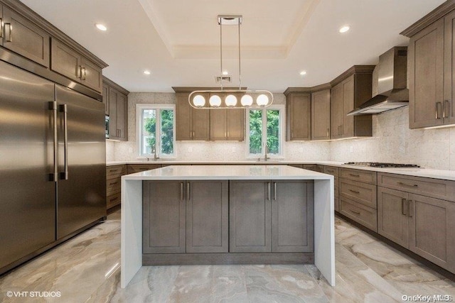 kitchen with hanging light fixtures, a center island, stainless steel appliances, and wall chimney range hood