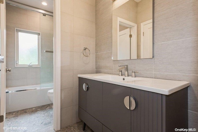 full bathroom featuring vanity, enclosed tub / shower combo, tile walls, and toilet