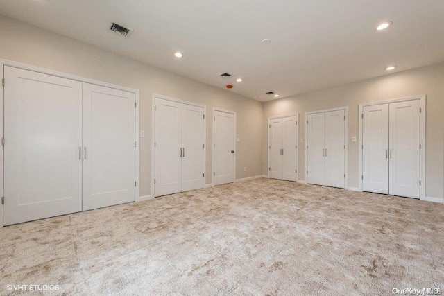 unfurnished bedroom with multiple closets and light colored carpet