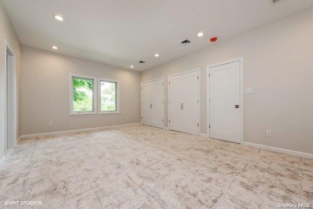 unfurnished bedroom with light colored carpet and multiple closets