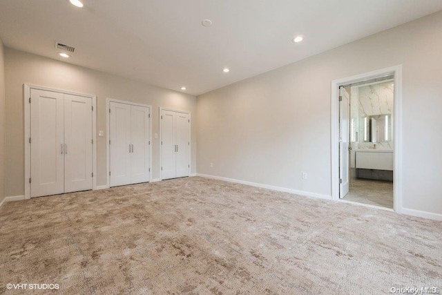 unfurnished bedroom with light colored carpet, ensuite bath, and multiple closets