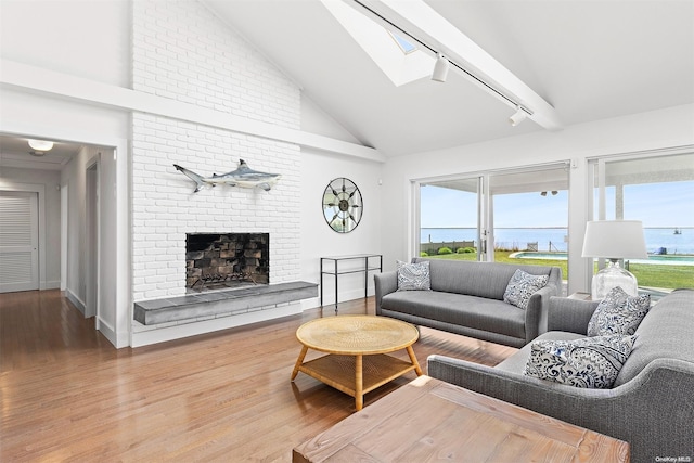 living room featuring track lighting, a water view, a skylight, a fireplace, and wood-type flooring