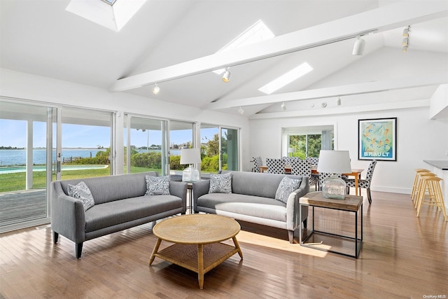 living room with a water view, light wood-type flooring, high vaulted ceiling, and track lighting