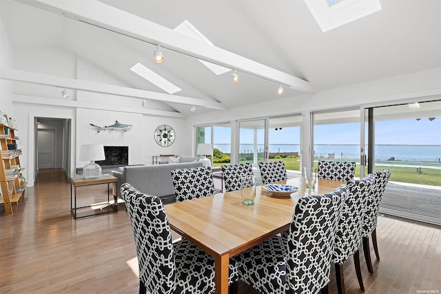 dining area with hardwood / wood-style floors, track lighting, a water view, a skylight, and a fireplace