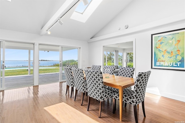 dining room featuring high vaulted ceiling, a water view, rail lighting, a skylight, and wood-type flooring