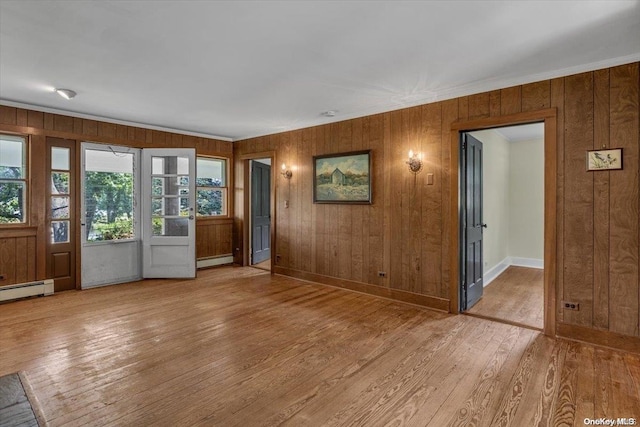 unfurnished living room featuring baseboard heating, wooden walls, light hardwood / wood-style flooring, and ornamental molding