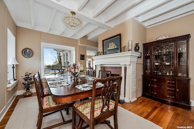 dining area featuring beam ceiling, a fireplace, dark wood-type flooring, and an inviting chandelier