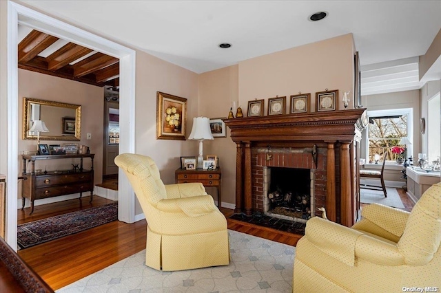 sitting room with hardwood / wood-style floors, beamed ceiling, and a brick fireplace