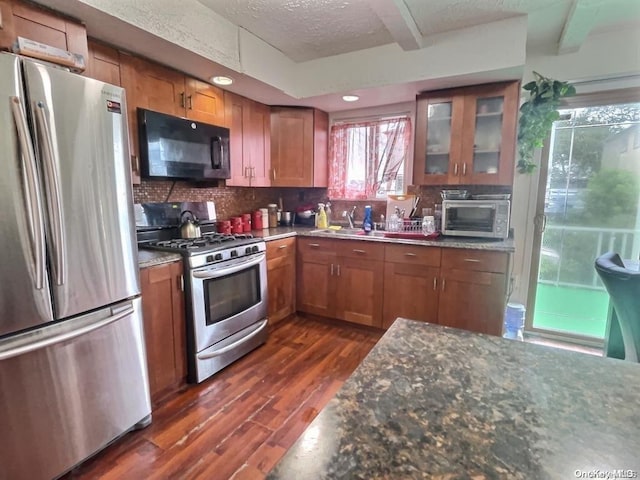 kitchen with stainless steel appliances, tasteful backsplash, dark hardwood / wood-style flooring, dark stone counters, and a textured ceiling