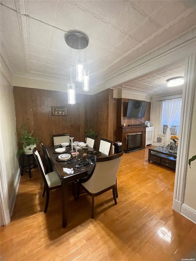 dining room with light wood-type flooring, ornamental molding, and wooden walls