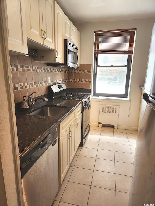 kitchen with sink, radiator heating unit, dark stone counters, decorative backsplash, and appliances with stainless steel finishes