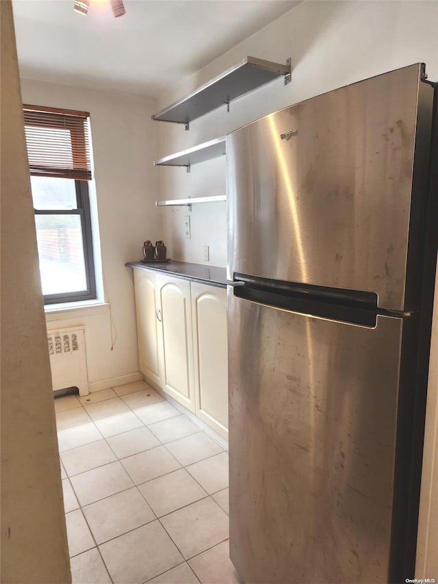 kitchen with stainless steel fridge, radiator heating unit, white cabinetry, and light tile patterned floors