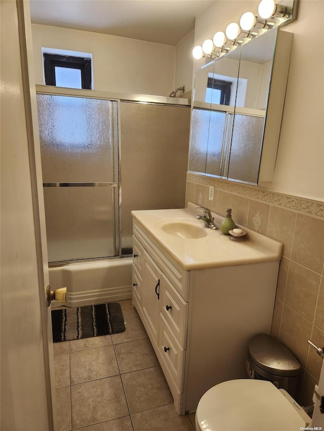 full bathroom with tile patterned flooring, enclosed tub / shower combo, toilet, vanity, and tile walls