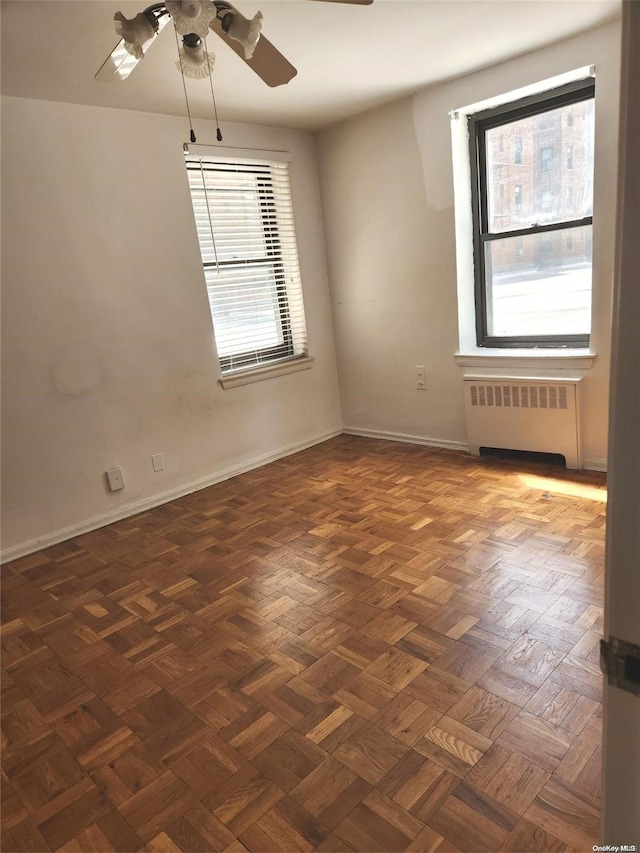 unfurnished room with ceiling fan, dark parquet flooring, and radiator heating unit