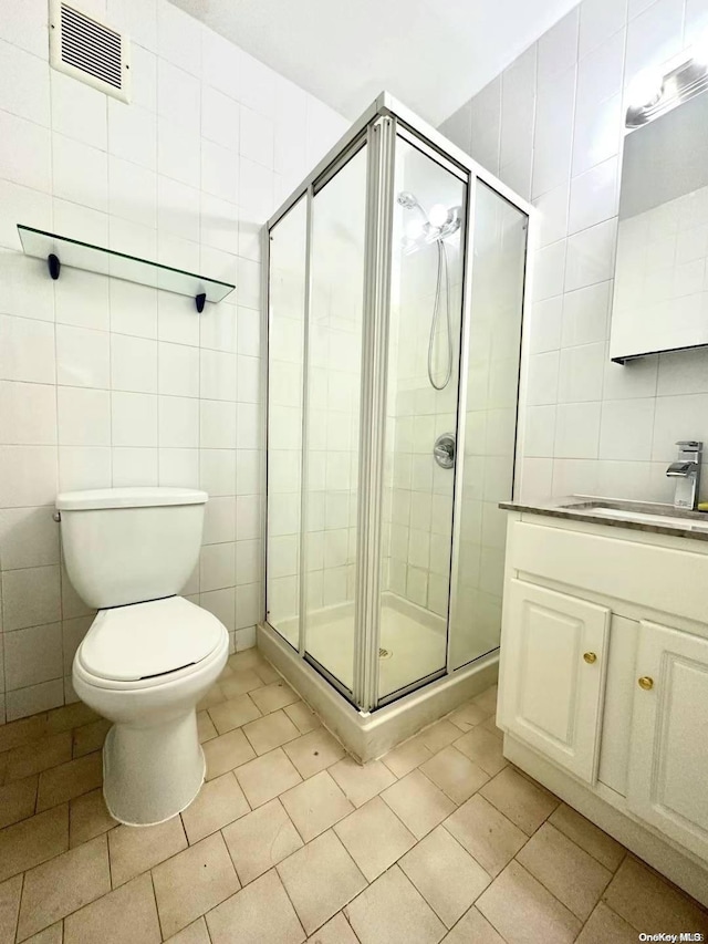 bathroom featuring vanity, toilet, tile walls, and a shower with shower door